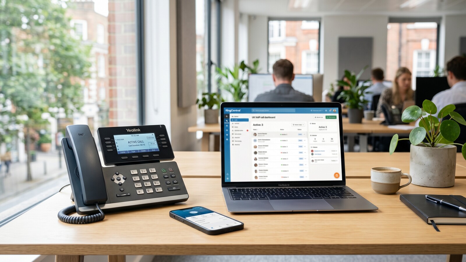 A modern VoIP desk phone next to a smartphone on a small business desk with a laptop showing a call dashboard